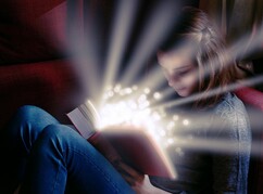 Auf einem Sofa sitzendes Mädchen mit einem Buch in der Hand und liest