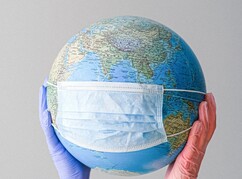 Weltkugel mit Maske von zwei Händen gehalten 