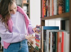 Mädchen in Bibliothek vor Bücherstapel - auf der Suche nach einem Buch