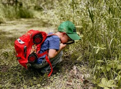 Bub mit Rucksack und Lupe hockend