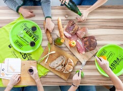 Holztisch mit Tellern, Aufdruck Sauberhafte Feste sowie Jause und Armen von vier...